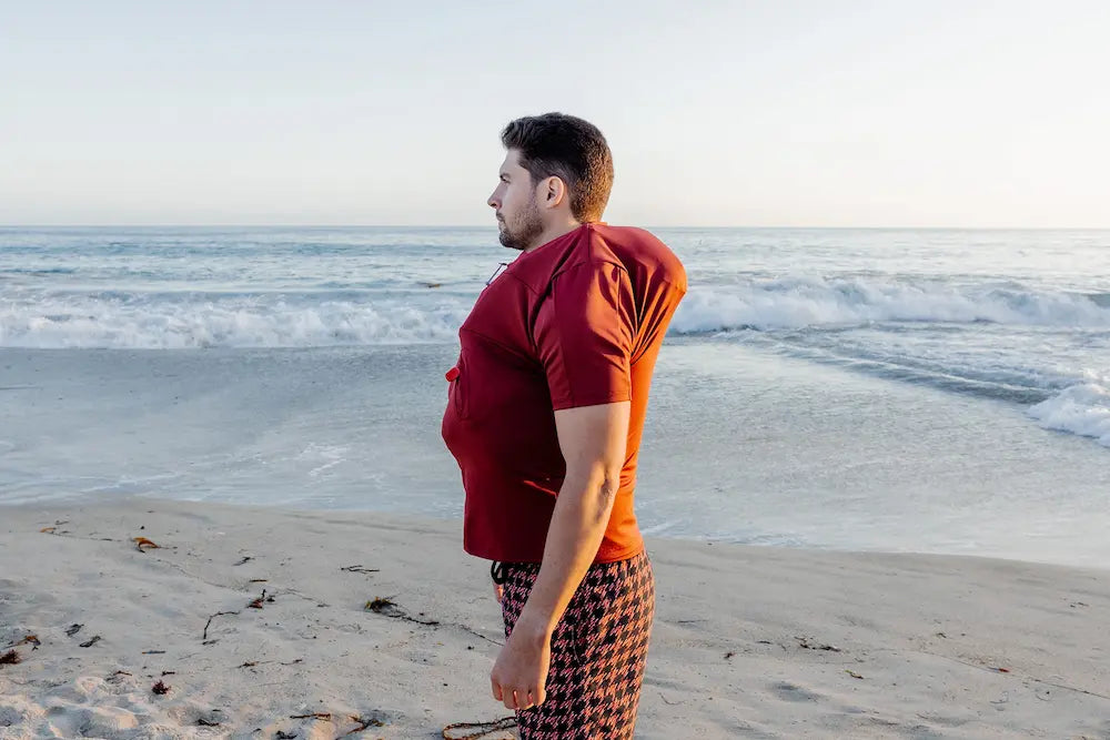 Homme sur une plage et portant le tee-shirt anti-noyade adulte automatique Floatee gonflé, manches courtes, rouge